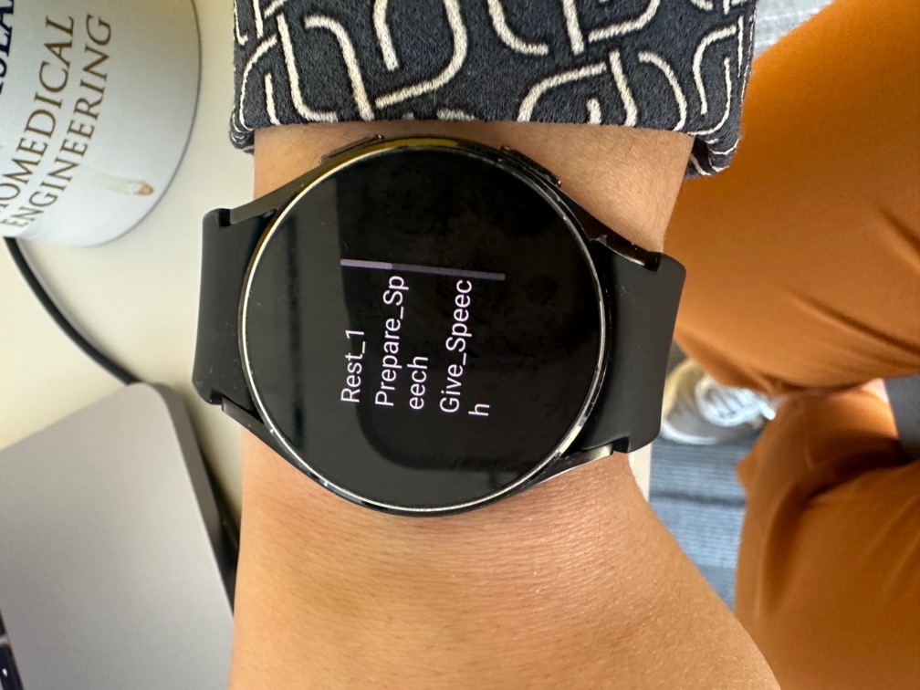 The watch worn on the wrist, stepping through the stress-test protocol: Rest 1, Prepare Speech, Give Speech.